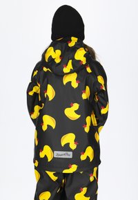 Schwarze Regenjacke mit gelben Gummienten-Mustern, ausgestattet mit einer Kapuze und elastischen Bündchen. Logosticker am hinteren Saum sichtbar.