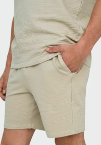 Camisa y pantalones cortos de textura beige claro, confeccionados en un tejido transpirable, con un corte relajado y bolsillos laterales para mayor comodidad.