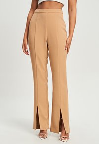 Tan hoge taille broeken met zijsplitten, taps toelopende pijpen, gladde stof en een schoon ontwerp. Heeft een platte tailleband en geen zichtbare sluitingen.