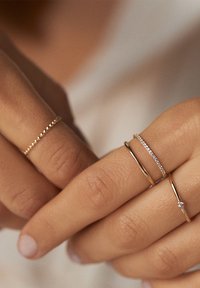 Des bagues en or sur des doigts ; trois styles : une bande perlée, une fine bande avec de petites pierres précieuses, et une bande lisse avec un seul accent en diamant.