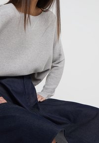 Pull en tricot gris avec un col large, associé à une jupe en denim bleu foncé taille haute. Texture douce, coupe décontractée et design simple.