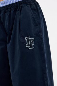 Calções azul-marinho feitos de tecido macio, com pregas, cintura elástica e logótipo "LF" bordado em cinza claro no lado esquerdo.