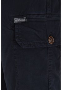 Pantalones cortos cargo de color azul oscuro, hechos de algodón, que cuentan con un bolsillo frontal con una solapa rectangular y un detalle de botón de madera. Costuras visibles.