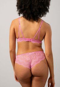 Roze kanten lingerie set bestaande uit een strappy bh en bijpassende slip. Opvallende gegolfde randen en intrigerende kantpatronen versterken het ontwerp.