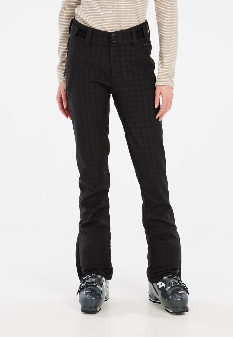 Crne skijaške hlače s uzorkom houndstooth, elastičnim pojasom i dva dugmeta. Uparene s sivim skijaškim čizmama za aktivnosti na otvorenom.