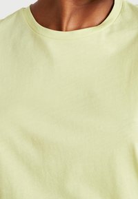 Jasnożółta bawełniana koszulka z okrągłym dekoltem i krótkimi rękawami. Gładka tekstura z delikatnym drapowaniem, bez widocznych wzorów lub akcentów.