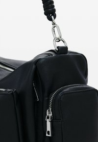 Zwarte leren tas met een gestructureerd oppervlak, meerdere ritscompartimenten en zilverkleurige hardware met een gedraaide schouderband.