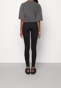 Vaqueros negros ajustados de cintura alta, diseño de cinco bolsillos y textura suave. Combinados con una blusa suelta gris de manga corta.
