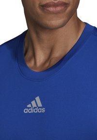 Blauw kortemouwen sportshirt van gladde stof, met een ronde hals en een opvallend grijs Adidas-logo op de borst.
