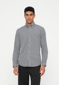 Černobílá kostkovaná košile na knoflíky s dlouhými rukávy, límečkem a malým detailem loga na hrudi. Hladký bavlněný materiál.