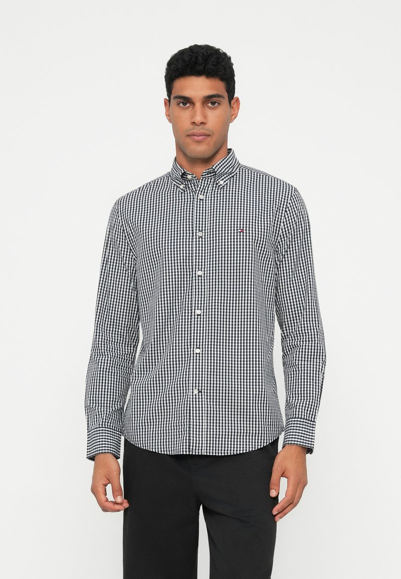 Černobílá kostkovaná košile na knoflíky s dlouhými rukávy, límečkem a malým detailem loga na hrudi. Hladký bavlněný materiál.