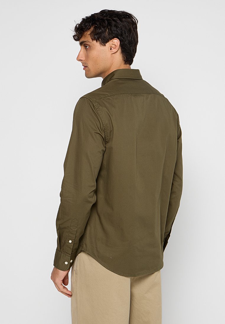 Camicia a maniche lunghe di colore verde oliva in un tessuto liscio, con colletto classico, orlo a camicia e polsini abbottonati.