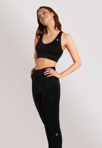 Reggiseno sportivo nero con un design frontale arricciato e logo, abbinato a leggings neri a vita alta con una consistenza liscia e elastica.
