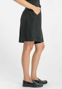 Jupe en jean noire, présentant une taille ajustée et deux poches latérales. Le design est longueur genou avec une coupe droite et des coutures minimales.