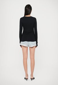 Top nero a maniche lunghe con design aderente, abbinato a pantaloni corti in denim azzurri. Il modello indossa sandali neri con tacco. Sfondo bianco semplice.