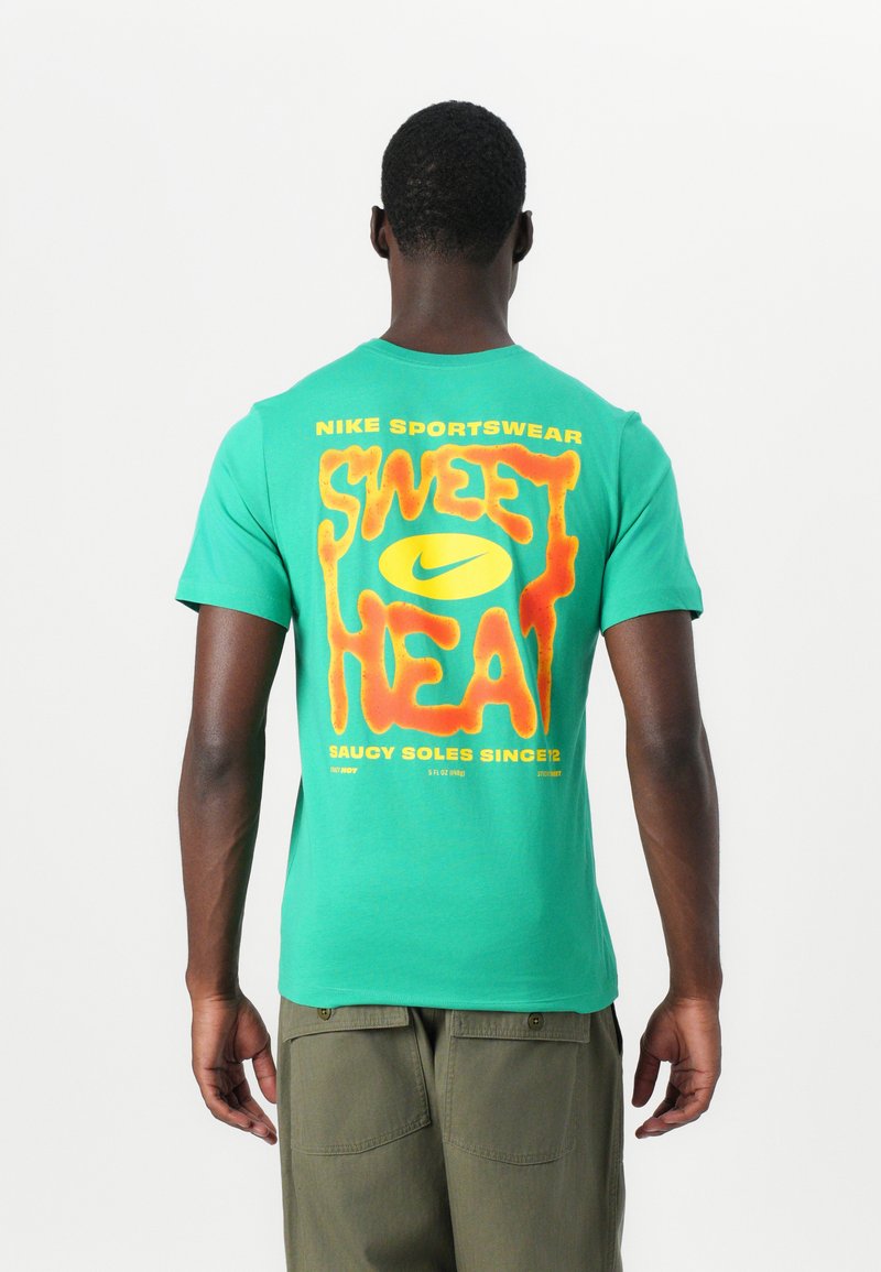 Grøn bomulds T-shirt med et stort orange og gult grafik på ryggen, der står "SWEET HEAT" med Nike logo og branding.