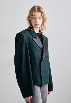 Dubbelknäppt blazer i mörkgrön ullblandning, har kontrasterande svarta slag, oversized axlar och stora knappar.