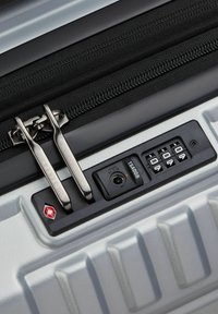 Valigia rigida argentata con lucchetto, zip nera, due tiranti metallici per la zip e un lucchetto a combinazione a tre cifre approvato TSA.