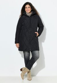 Svart vadderad parka med huva, med en främre dragkedja och tv�å sidofickor. Kombinerad med mörka jeans och beigefärgade ankelstövlar.