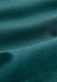 Texturiertes Gewebe in tiefem Teal mit einem subtilen geometrischen Muster. Das Material wirkt glatt und leicht reflektierend und zeigt sanfte Falten.