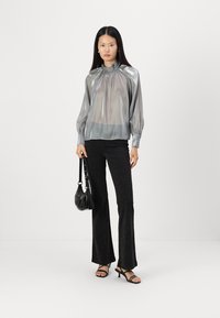 Blusa argentata trasparente con scollatura arricciata e maniche lunghe; abbinata a pantaloni neri a zampa d'elefante con un delicato luccichio; borsa nera e tacchi.