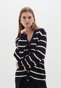 Marinblå och vit randig kofta med V-hals, långa ärmar och sex knappar framtill. Mjuk stickad textur.