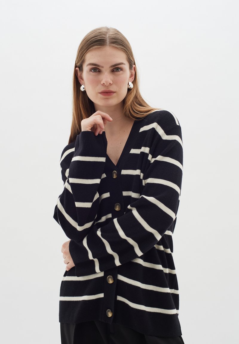 Marinblå och vit randig kofta med V-hals, långa ärmar och sex knappar framtill. Mjuk stickad textur.