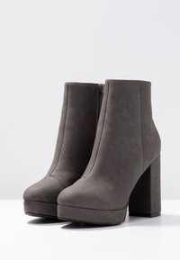 Harmaat nilkkakengät, joissa on korkea, tukevampi korko. Valmistettu sileästä synteettisestä materiaalista, sivuvetoketjulla ja pyöreällä kärjellä. Littee pohja.