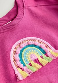 Sweat-shirt rose avec un arc-en-ciel brodé coloré comprenant des pompons et des glands en fils roses, jaunes, verts et turquoise.