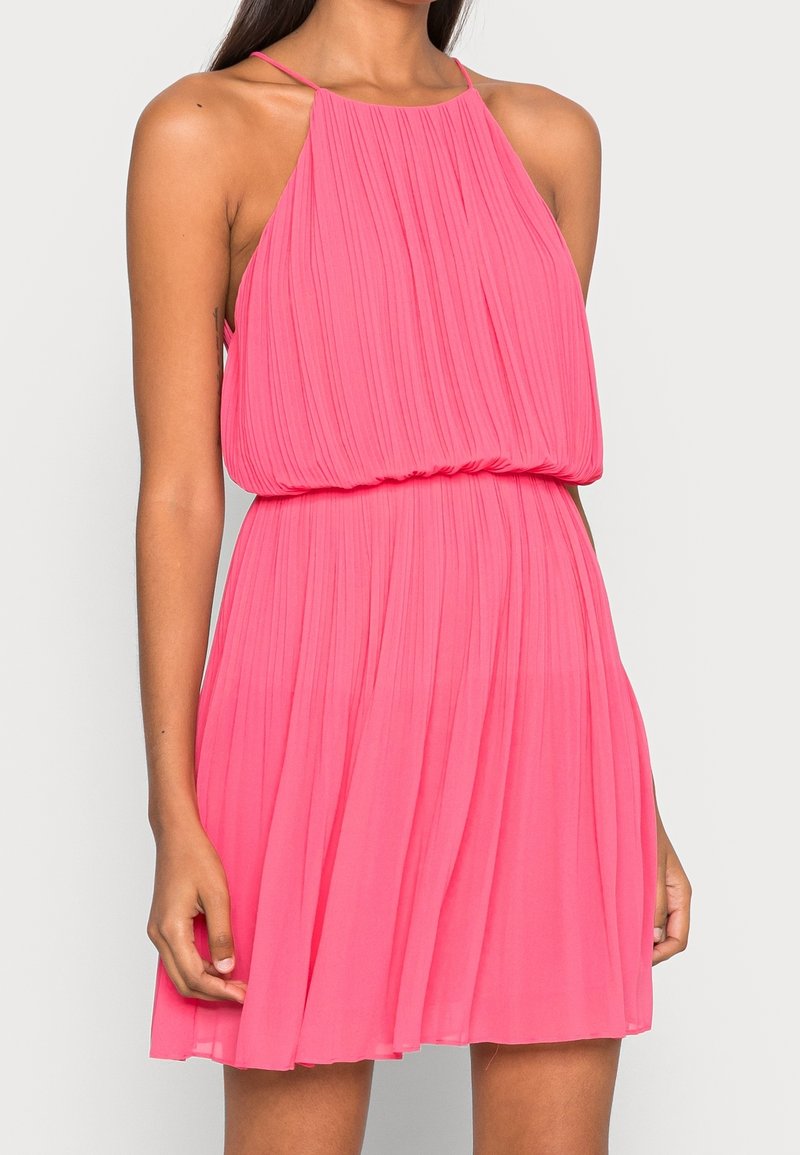 Robe plissée rose avec col licou, corsage ajusté et jupe fluide. Confectionnée dans un tissu léger, dotée de bretelles délicates.