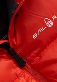 Rode gewatteerde jas met een strak ontwerp, zwarte rits met een trekband en het "SAIL"-logo in het wit. Glad, glanzend stofoppervlak.