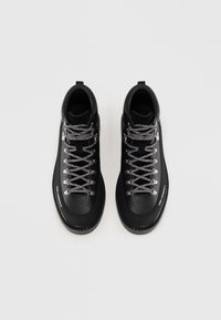 Botas de senderismo negras con un exterior sintético, ojales metálicos, cordones grises texturizados y una suela de goma con un diseño de fondo.