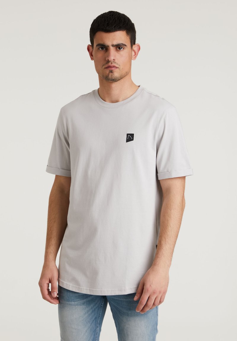 Tricou scurt cu manșon scurt, de culoare gri deschis, realizat din bumbac; prezintă mâneci răsucite și un mic patch cu logo negru pe piept.