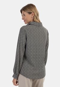 Camicia a maniche lunghe nera con un motivo floreale bianco, dotata di colletto, polsini bottonati e orlo curvo. Tessuto morbido.