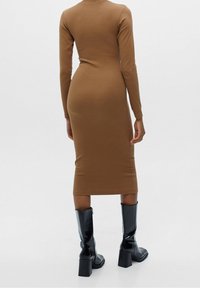 Robe midi moulante en tissu marron, à manches longues, au design ajusté, avec un ourlet droit et des bottes en cuir noir montant au genou.
