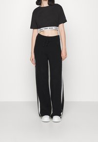 Svart kort t-shirt med vit logotypsmudd, matchad med svarta vidbeniga sweatpants med vita sidoremsor. Vita sneakers fullbordar looken.