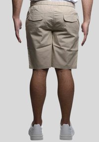 Pantaloni beige con una vita elasticizzata, due tasche posteriori e una texture liscia. Indossati con sneakers bianche, visti da dietro.