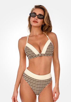 Mujer con bikini de tiro alto con patrón geométrico en tonos marrón y crema, top triangular y gafas de sol ovaladas negras, sobre fondo blanco.
