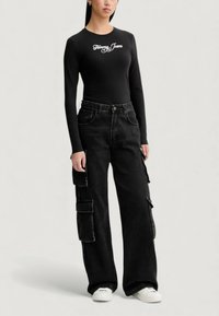 Czarna koszula z długim rękawem z logo „Tommy Jeans”, zestawiona z szerokimi czarnymi spodniami typu cargo z bocznymi kieszeniami oraz białymi trampkami.