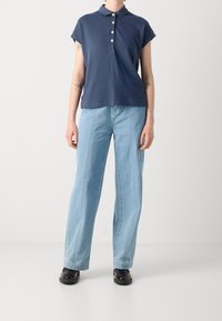 Polo bleu marine avec col et patte de boutonnage, associé à un jean clair à jambe large et des chaussures noires. Tissu lisse et coupe décontractée.