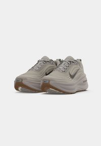 Pair of beige Nike ZoomX running shoes with thick cushioned soles and black swoosh logos on a white background.