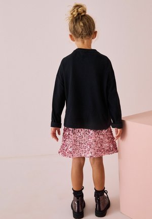 Schwarzes Langarmshirt kombiniert mit einem rosa Paillettenrock und schwarzen Stiefeletten. Das Outfit zeichnet sich durch ein lässiges Design und glänzende Texturen aus.