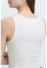 Valkoinen puuvillainen tanktoppi, jossa on slim fit -muoto, leveät olkaimet ja sileä pinta. Siinä on pyöreä pääntie ja minimaaliset saumat.
