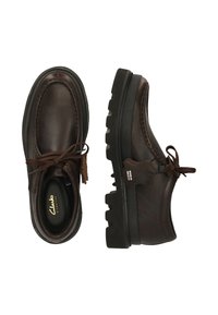 Scarpe in pelle marrone scuro con lacci, dotate di suole in gomma nera spessa, una scarpa vista dall'alto e l'altra di lato che mostra le cuciture e l'etichetta.