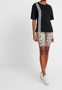 Czarny t-shirt z krótkim rękawem w białe ukośne paski, zestawiony z beżowymi szortami rowerowymi w leopardzie i białymi trampkami. Gładka tekstura materiału.