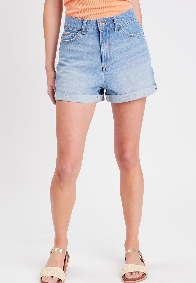 Pantalones cortos de mezclilla azul claro con una cintura alta, dobladillos enrollados, dos bolsillos frontales y cierre de botón. Textura suave con ligero desvanecimiento.