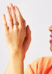 Metalring med lilla og gule striber, båret på en hånd, der viser glat tekstur og rund form. Hudfarven er synlig nedenunder.