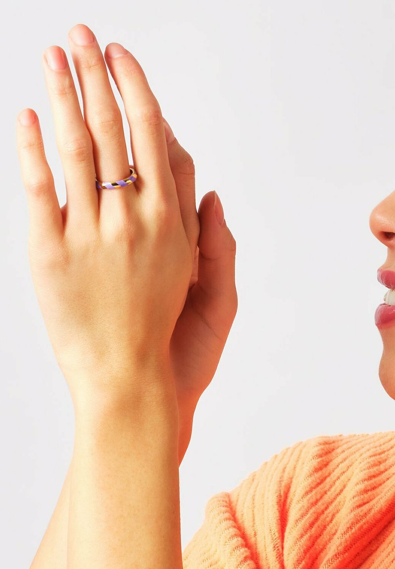 Metalring med lilla og gule striber, båret på en hånd, der viser glat tekstur og rund form. Hudfarven er synlig nedenunder.