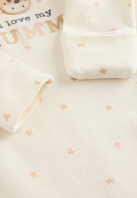 Kreemikas beebiriietus pikkade varrukatega, millel on tikitud loomamotiiv ja pehmed tähe mustrid õrnroosas toonis.