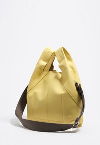 Żółta skórzana torba o luźnym kształcie, z dwiema górnymi rączkami i brązowym plecionym paskiem. Posiada pionowe przeszycia i gładką teksturę.